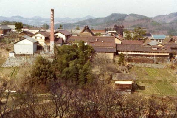 Wide view of the brewery complex with its brick chimney, nestled in the mountains.