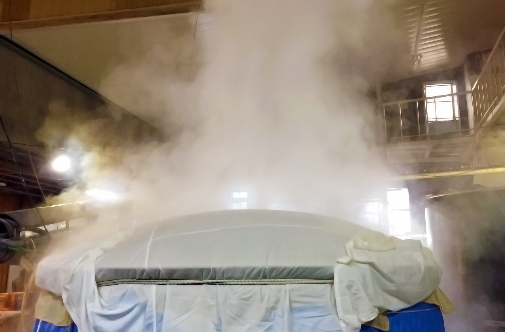 Steam billowing above a covered rice-steaming vat inside the brewery building.