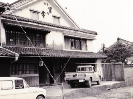 Historical photograph of the Koimari Shuzo brewery building and vintage delivery truck.