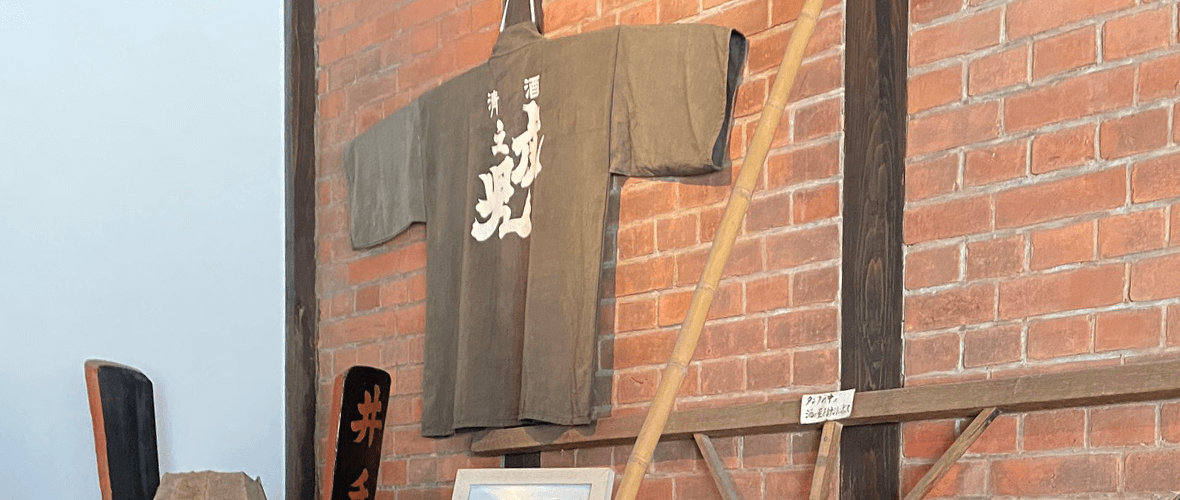 Brewery interior display with a Toranoko happi coat and historical brewing tools against a brick wall