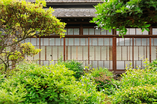 Traditional brewery building with lattice windows, seen through garden greenery.