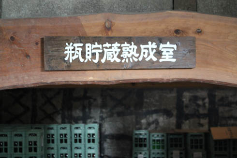 Sign reading "Bottle storage and aging room" above stacked crates of bottled sake