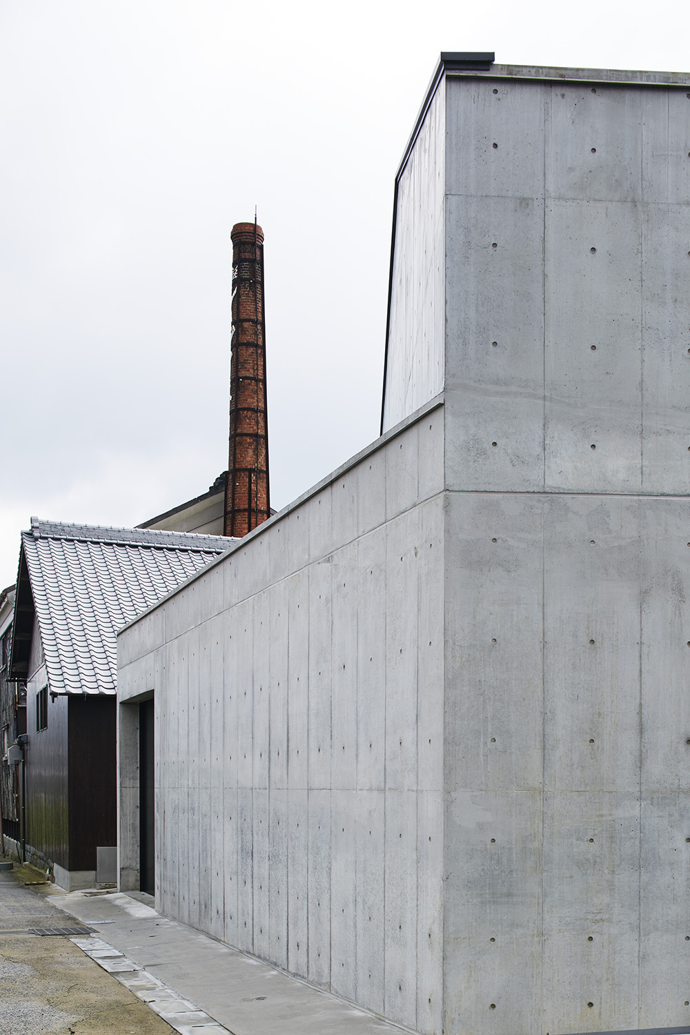 Corner view of the brewery's modern concrete annex with the brick chimney in the background.