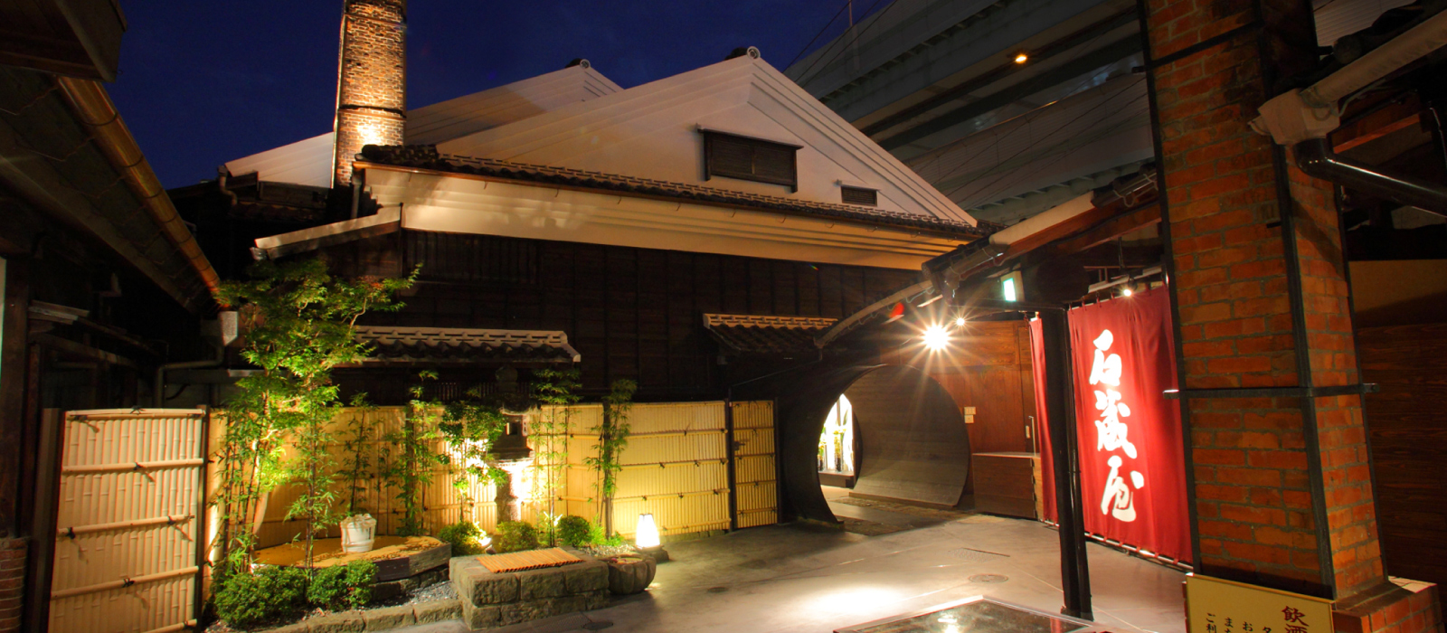 Night view of the brewery entrance with its distinctive circular wooden gate.
