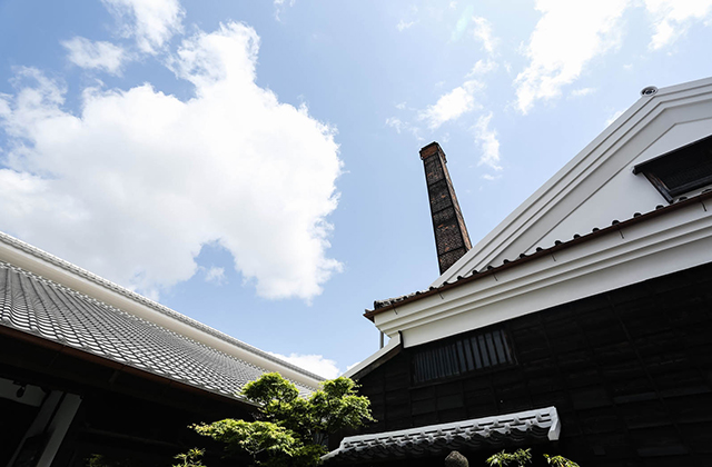 Upward view of the brewery roofline and chimney against a clear blue sky.