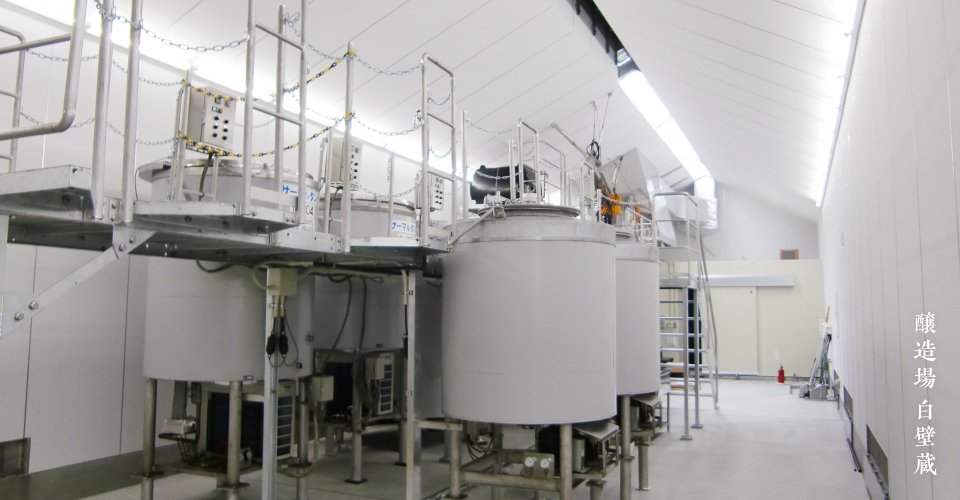 Interior of the Shirakabe-gura brewing facility showing fermentation tanks.