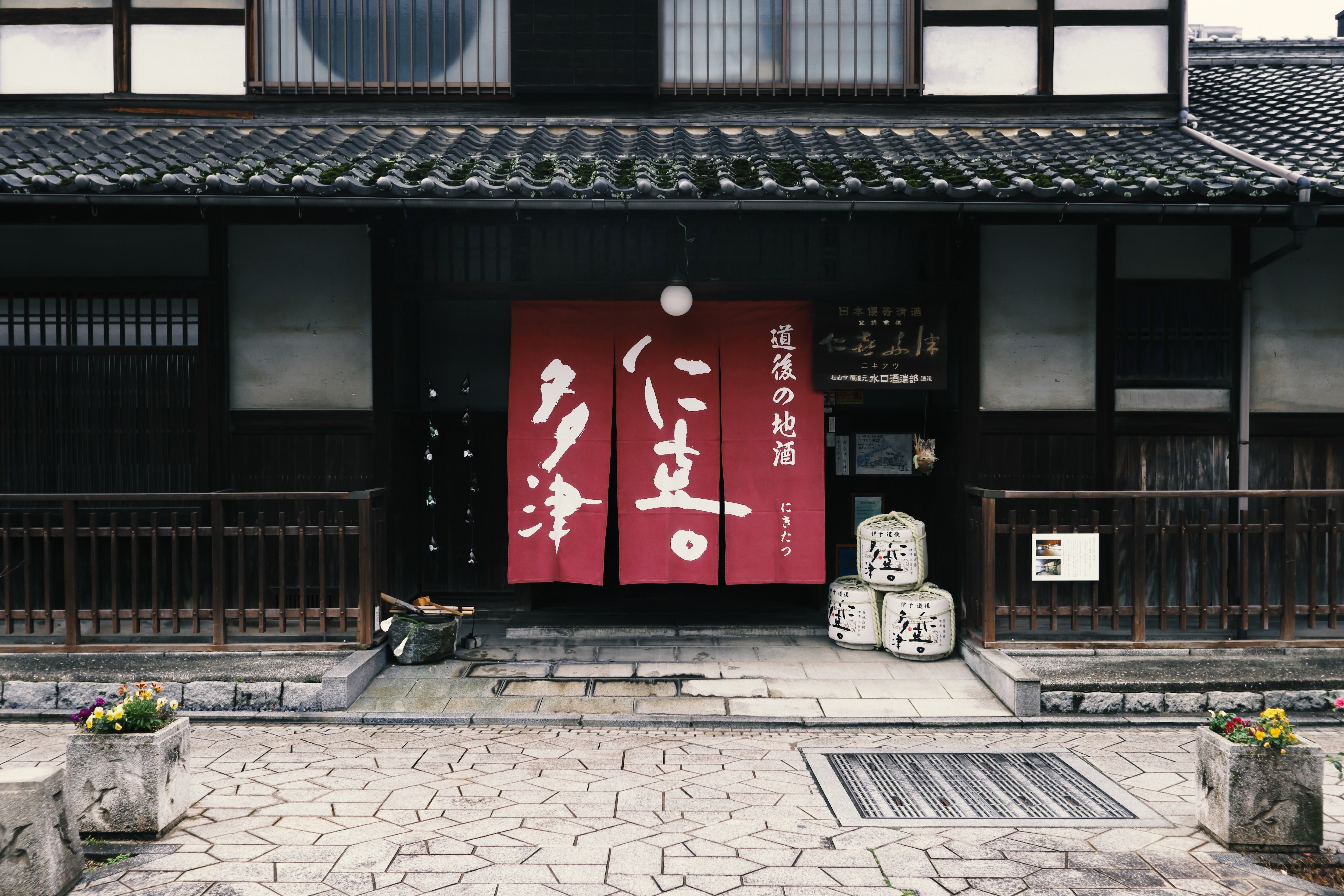 Storefront entrance with the Nikitatsu noren curtain and sake barrels.