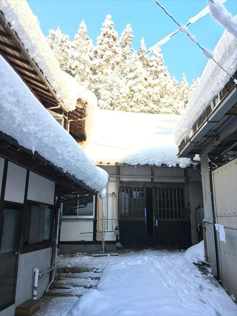 Snow-covered courtyard between the brewery's traditional wooden buildings in winter.