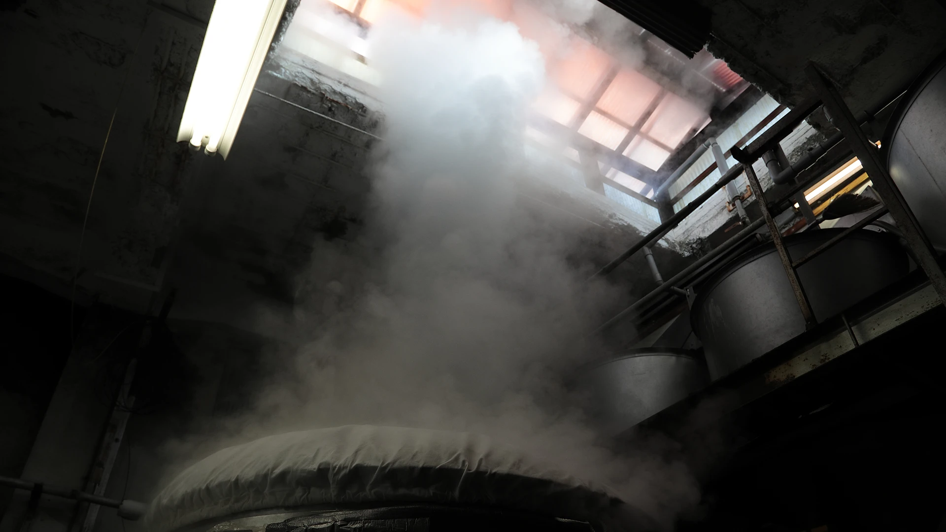 Steam rising above brewing tanks inside the kura
