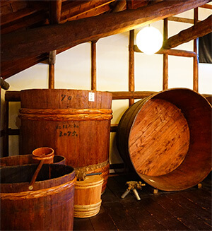 Traditional wooden fermentation vats and straw-wrapped barrels inside the old brewing hall