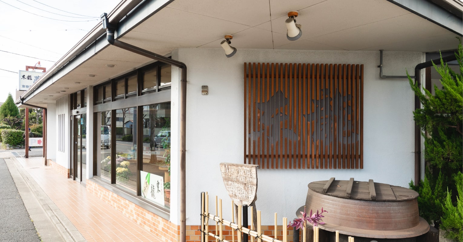Storefront entrance of the brewery office with the Azumaryu dragon emblem and a sake barrel display.