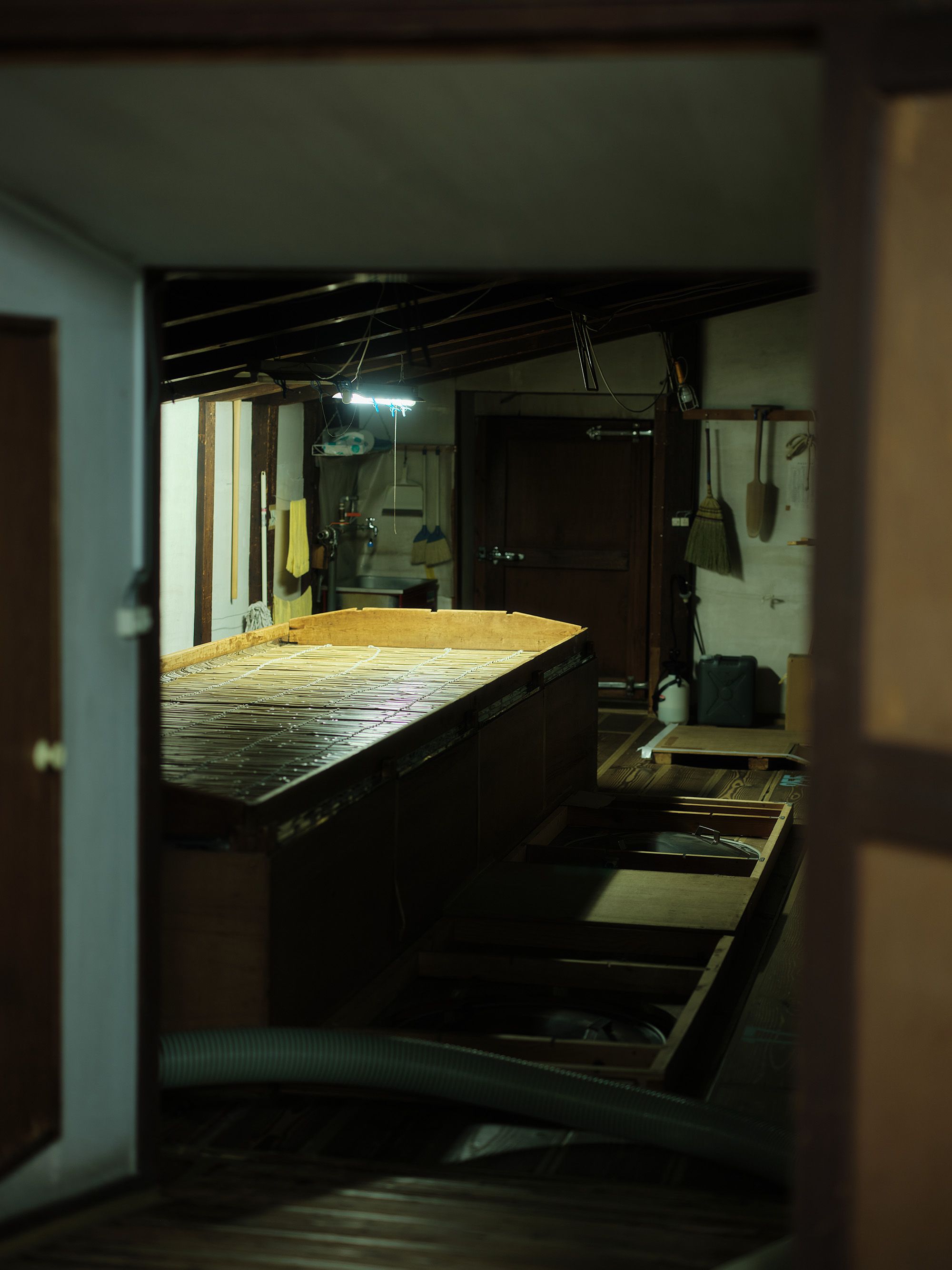 A traditional sake press (fune) used to separate sake from the lees, seen through a doorway in the brewing hall.