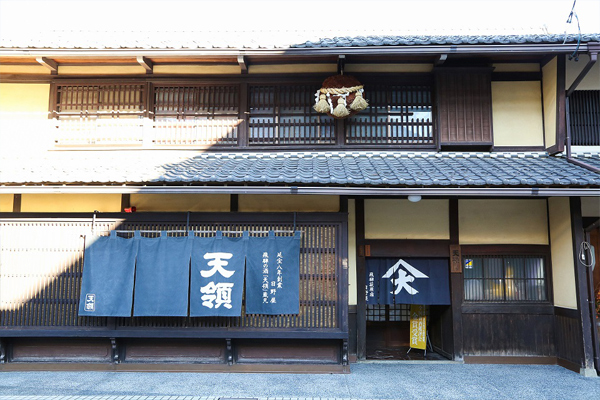 Street-facing facade of the shop with a dark blue noren curtain reading 'Tenryo' and a traditional sugidama cedar ball.