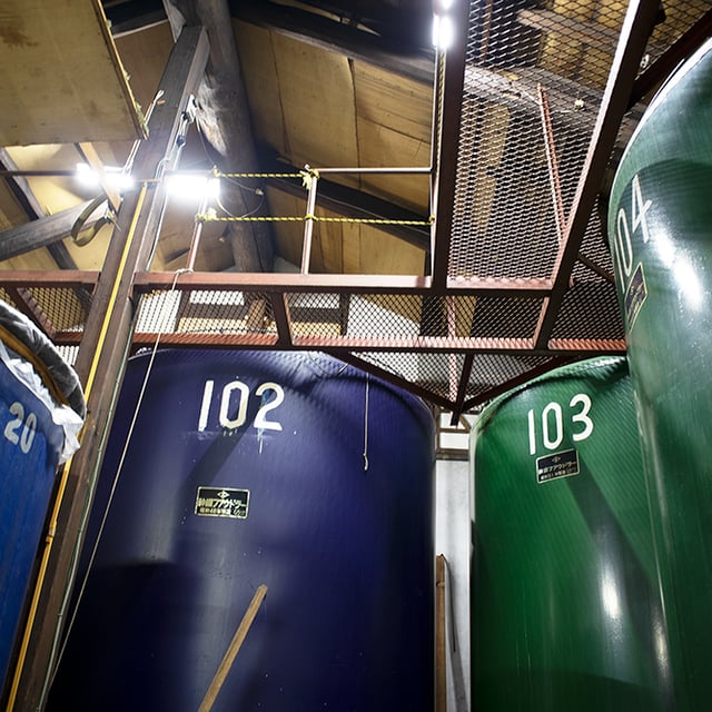 Numbered fermentation tanks (102, 103) beneath a catwalk inside the brewery