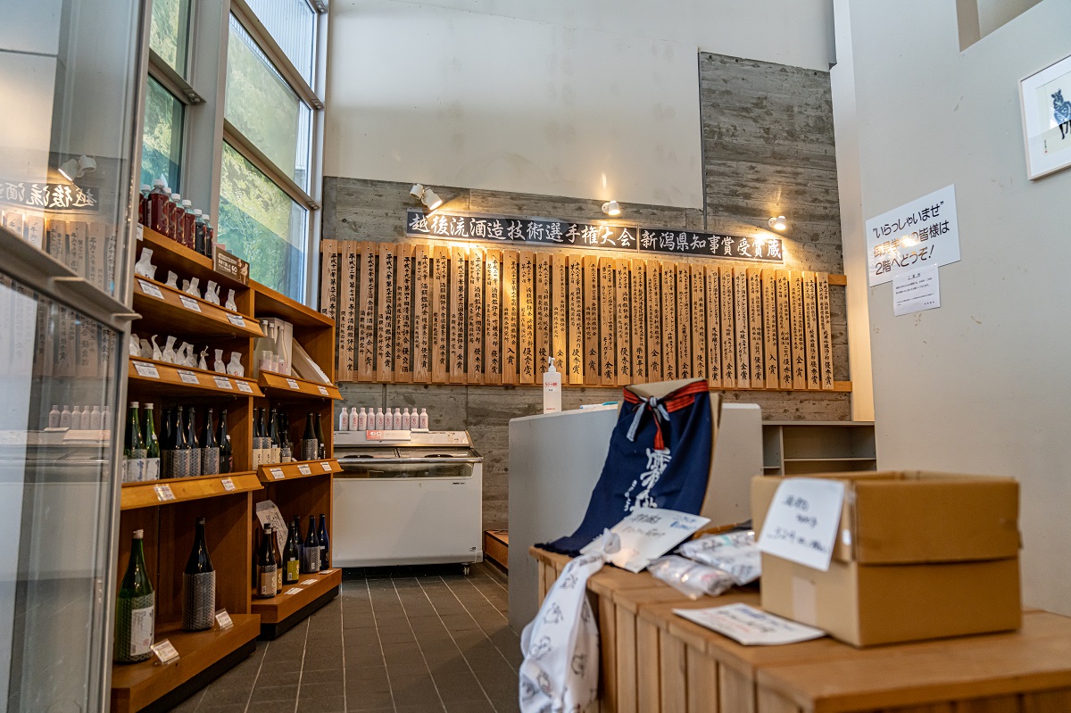 Brewery shop interior displaying sake bottles beneath a wall of competition award plaques.