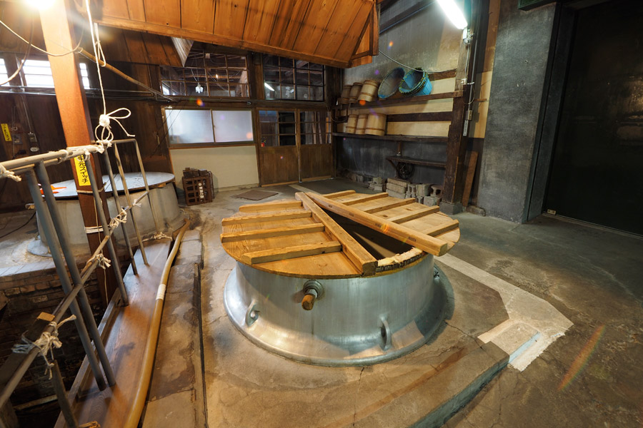 A stainless steel fermentation tank inside the brewing hall, with wooden lid boards laid across it.