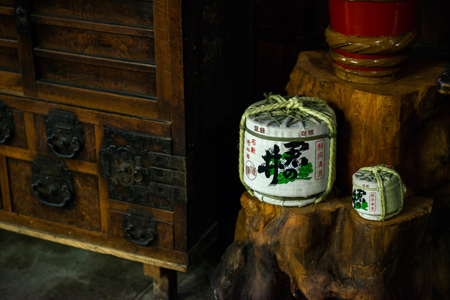 A traditional straw-wrapped sake barrel (taru) displayed beside an antique wooden chest inside the brewery.