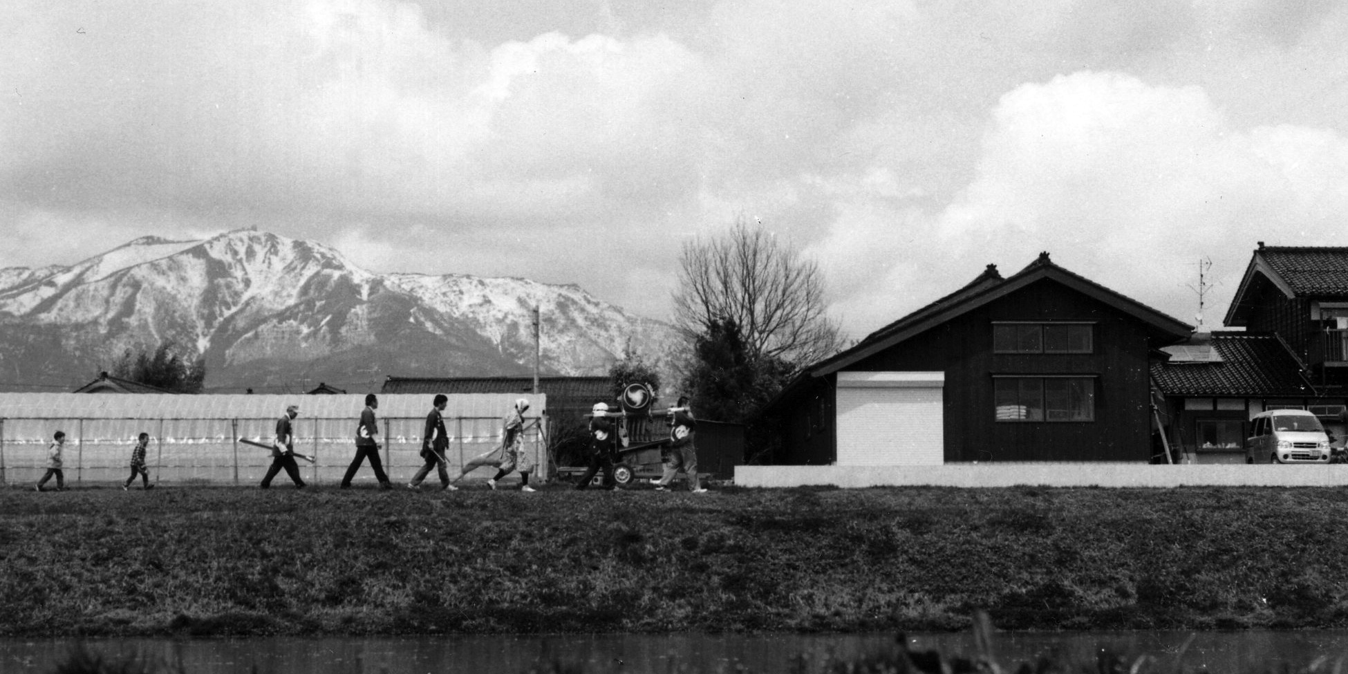 Snow-capped mountains rise behind rice paddies and farmhouses in the Sado countryside.