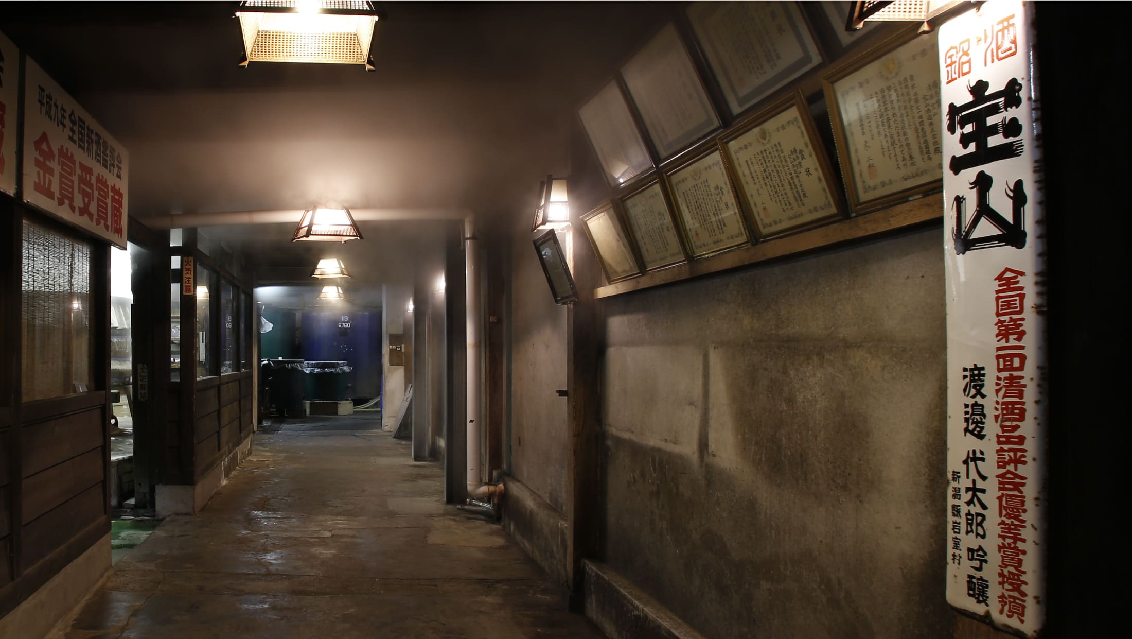 Interior corridor of the brewery lined with framed sake competition award certificates beneath the brewery's sign.