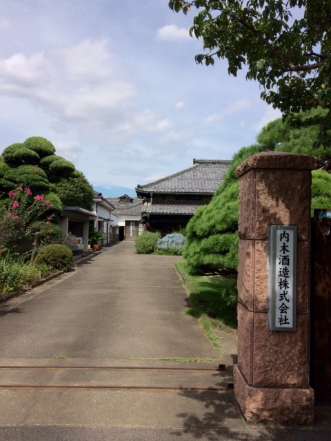Stone gate post engraved with the Uchiki Sake Brewery name, brewery building visible behind