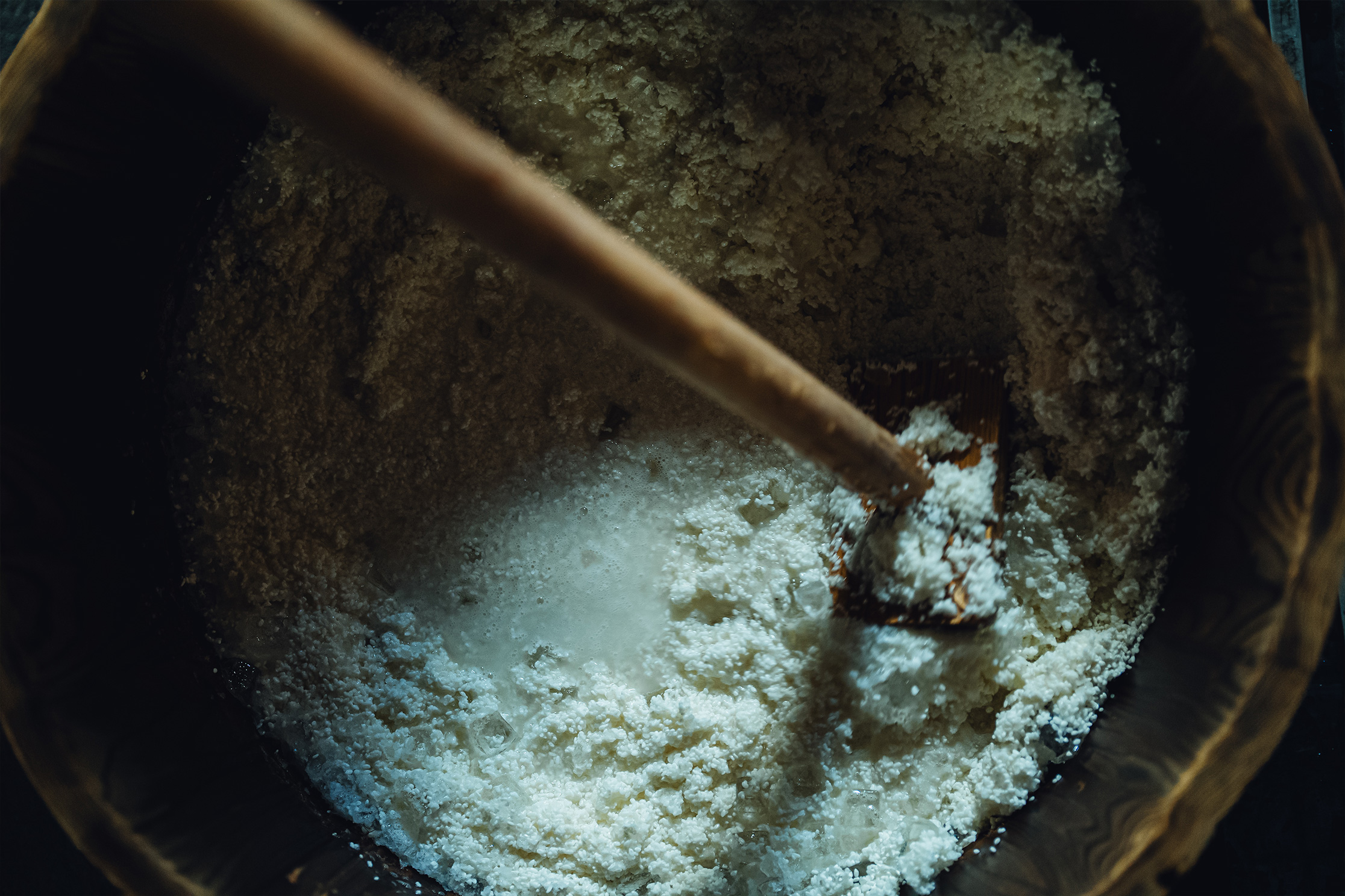 Close-up of steamed rice and koji being mixed in a wooden vat.