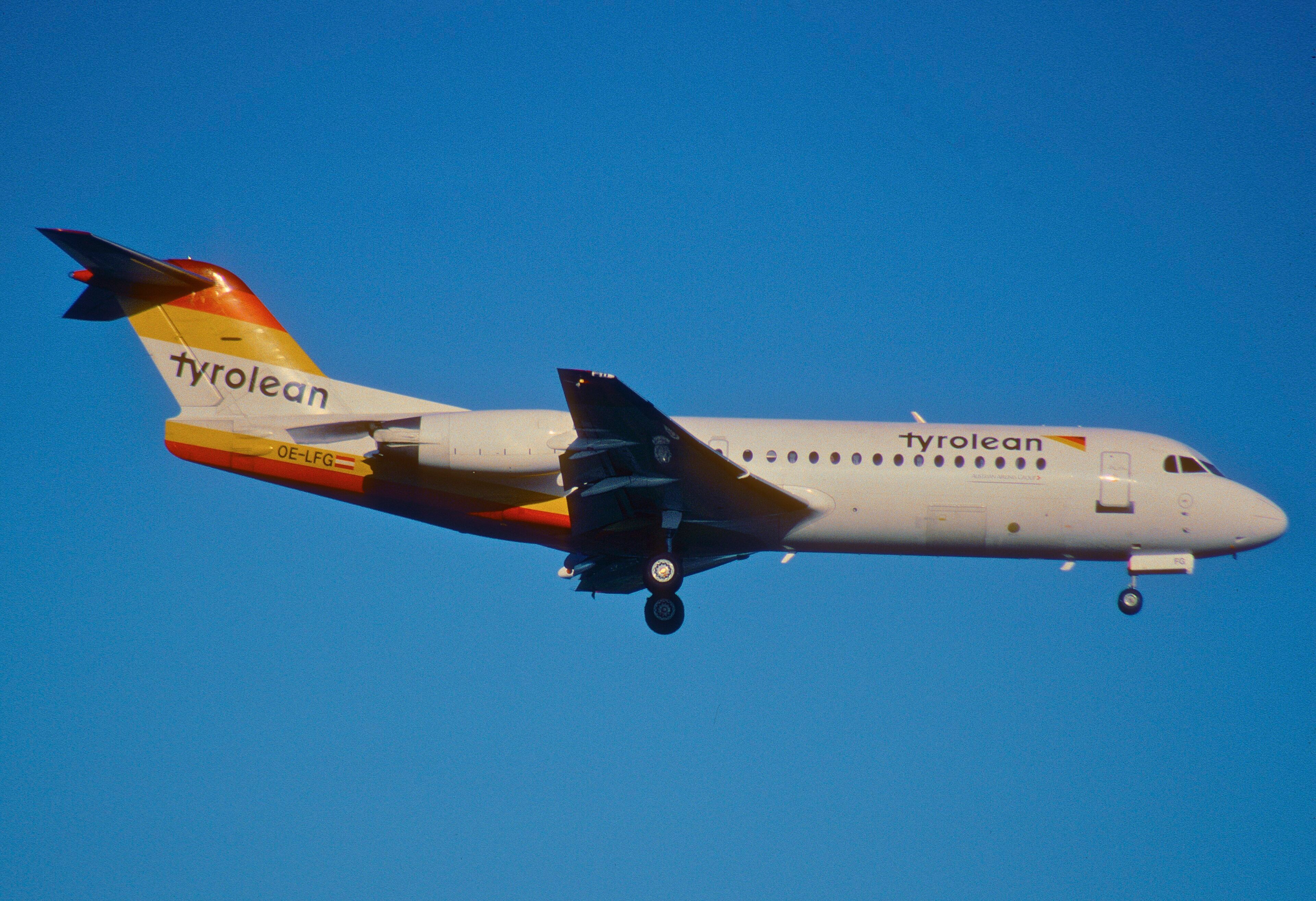 Ein Flugzeug der Tyrolean Airways, Kennung OE-LFG, im Landeanflug mit ausgefahrenem Fahrwerk vor klarem blauem Himmel.