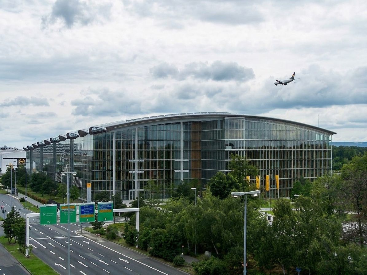 Lufthansa-Gebäude in der Nähe des Frankfurter Flughafens, Flugzeug startet, bewölkter Himmel.