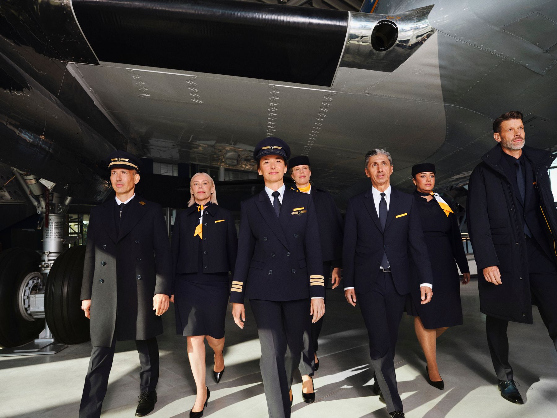 Lufthansa pilots and cabin crew model new BOSS-designed uniforms, walking together in an aircraft hangar.
