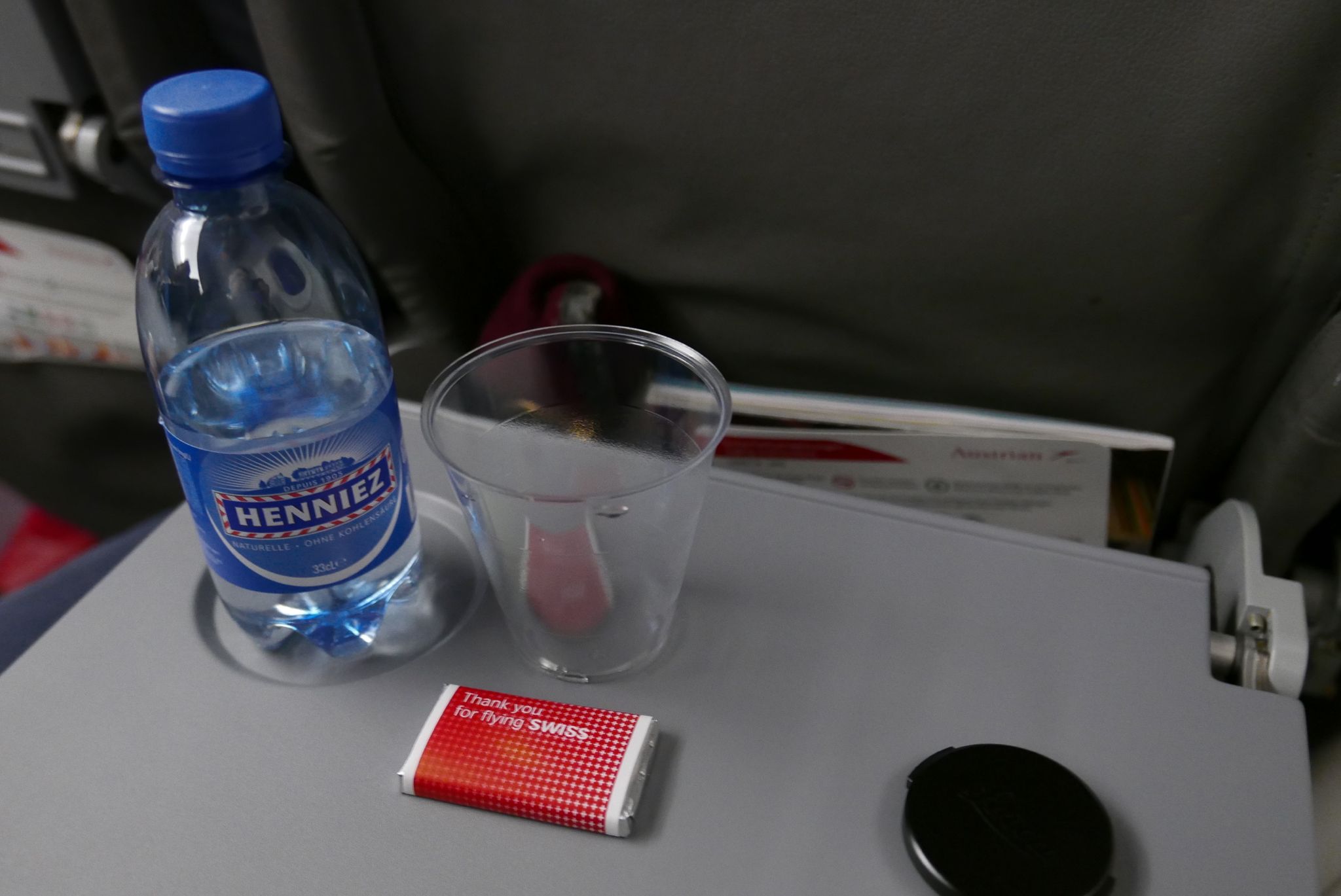 Airline tray table featuring water, a Swiss chocolate, and cup on an Austrian flight.