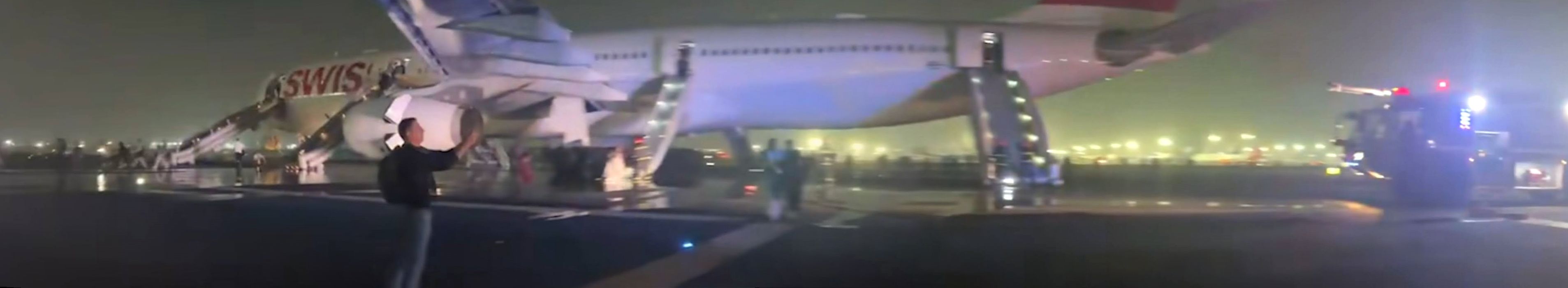 Passengers evacuate a SWISS airliner on the Delhi airport runway at night using slides while emergency vehicles surround the plane.