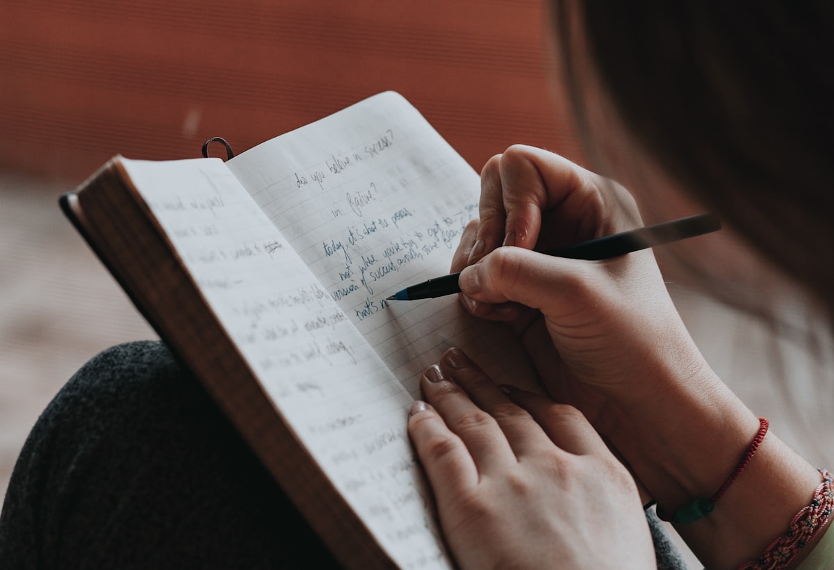 A person writing questions in a notebook before a care visit.