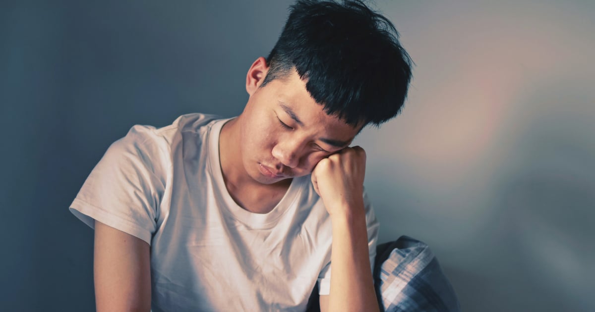 Personne allongée sur un canapé, l’air épuisé, avec un ventilateur et un verre d’eau à la main, symbolisant la fatigue après la canicule.