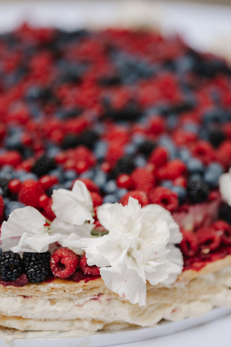 Nahaufnahme von Blaubeeren Himbeeren Brombeeren und weissen Blumen auf Kuchen
