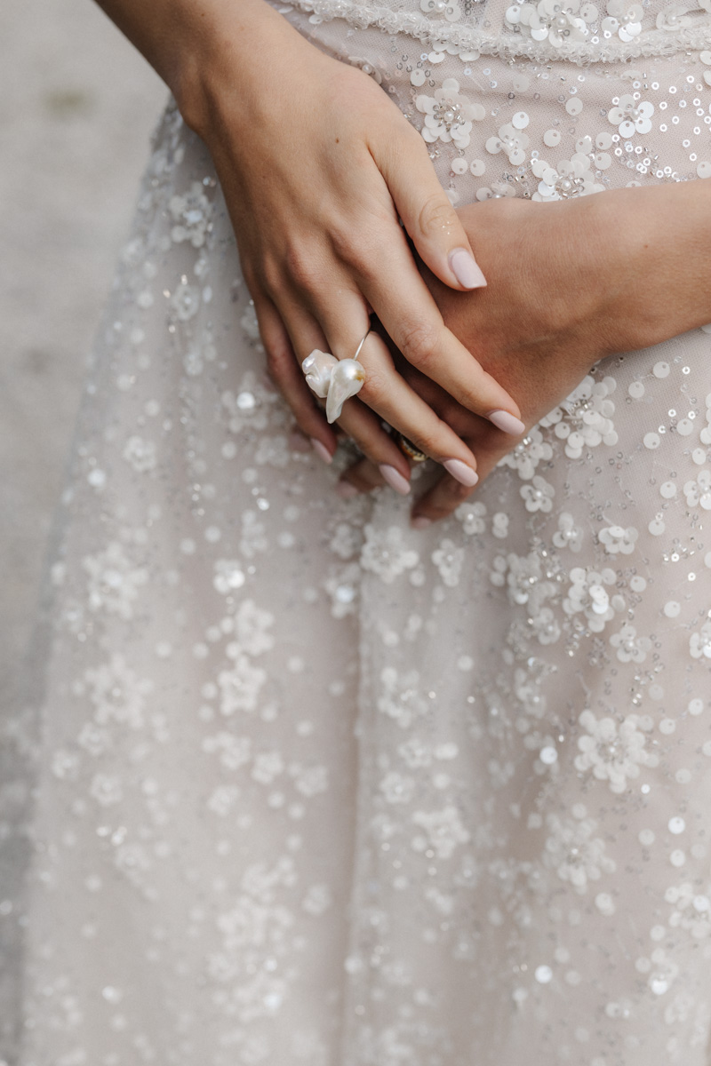 Hände mit Perlenring und Kleid mit Pailletten und Blumenmuster