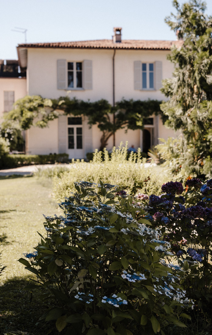 Garten mit Hortensien und Rasen vor einem hellen Gebäude mit Fensterläden