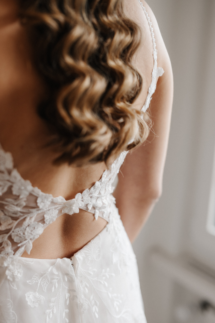 Frau mit blonden Locken und weissem Kleid mit Spitze am Rücken