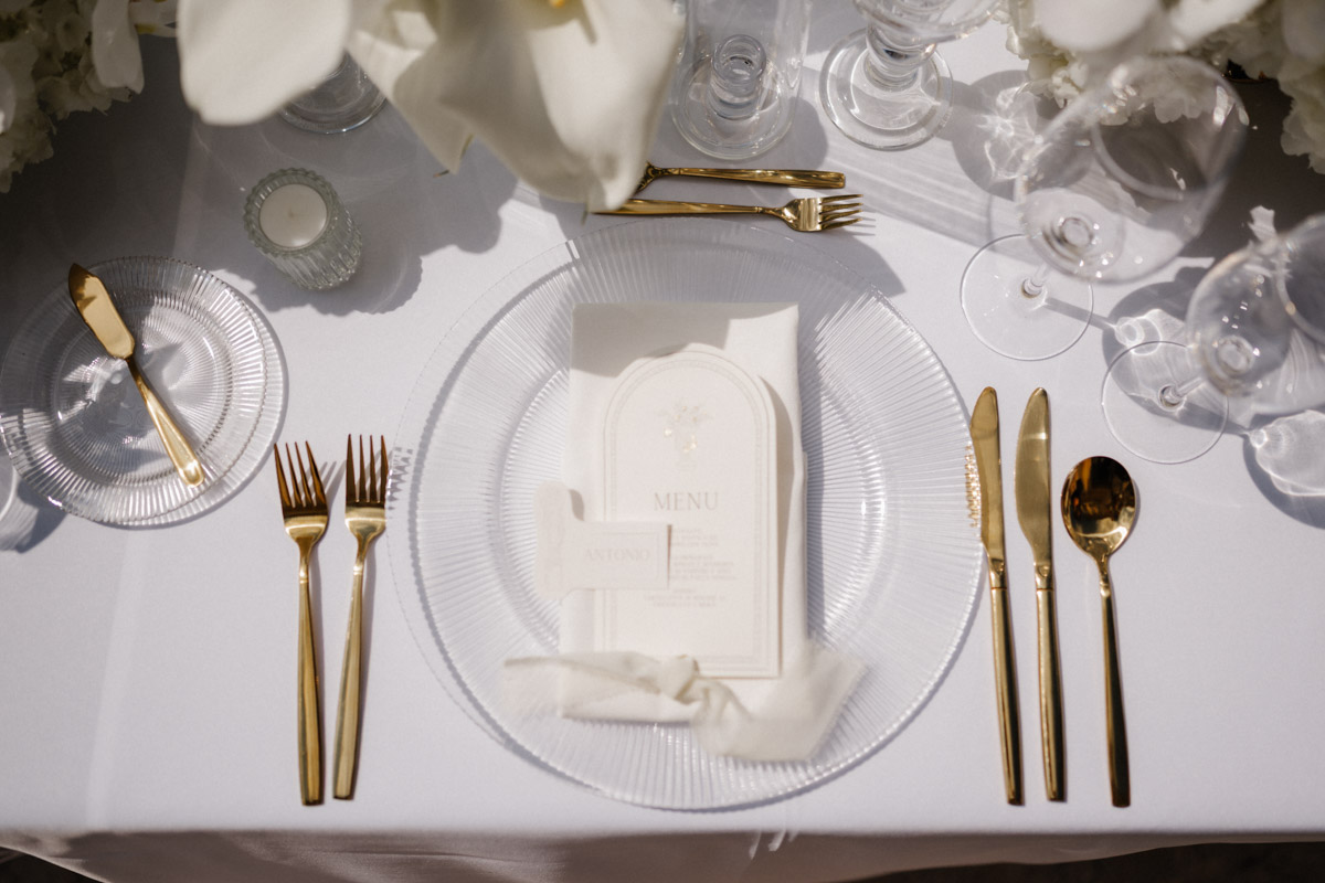 Gedeckter Tisch mit goldenem Besteck Menükarte und weissen Blumen