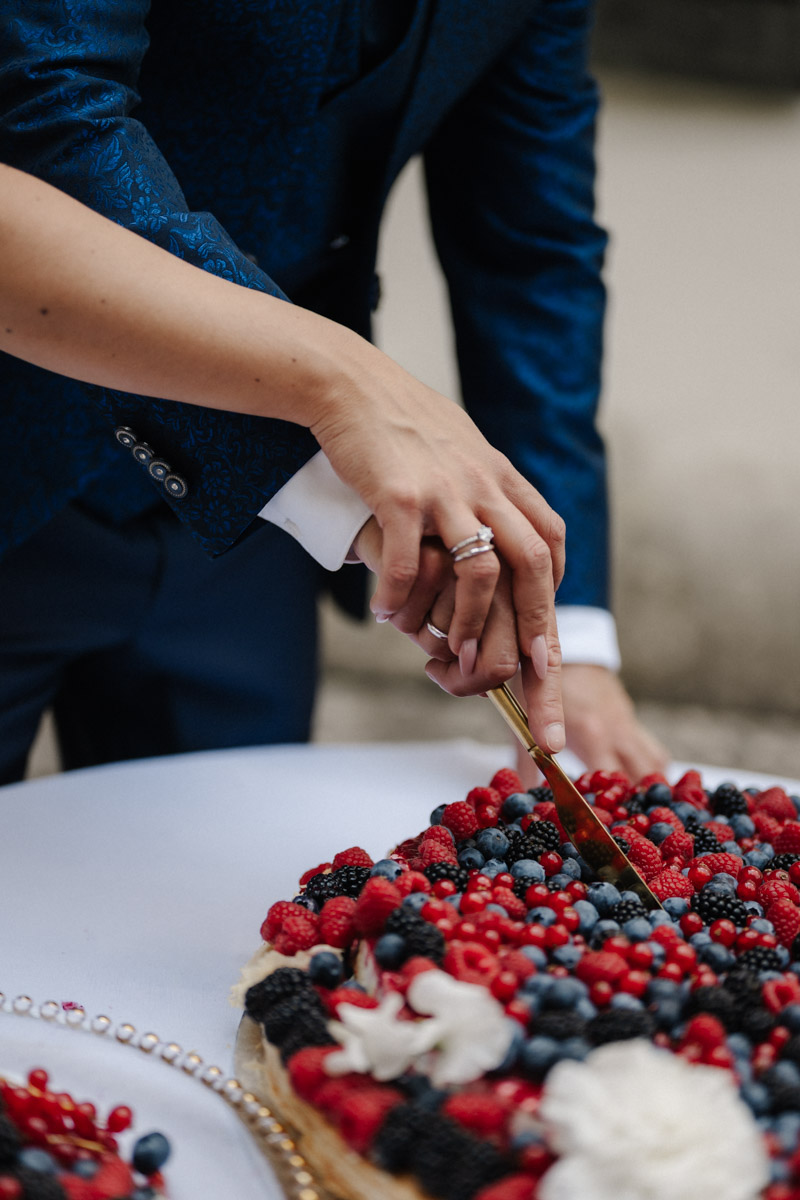 Brautpaar schneidet festliche Hochzeitstorte mit frischen Beeren bei Hochzeitsfeier an