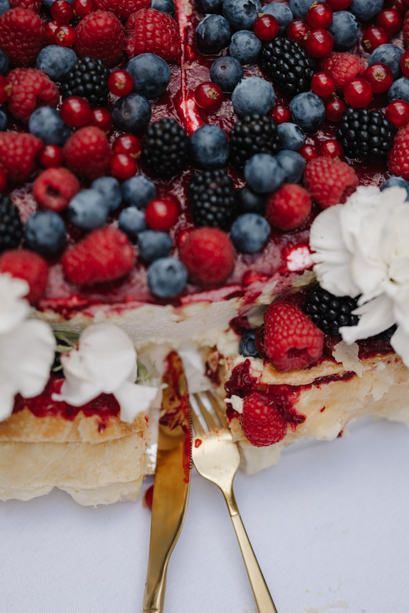 Elegante Hochzeitstorte dekoriert mit frischen Beeren und goldenem Besteck auf festlicher Tafel