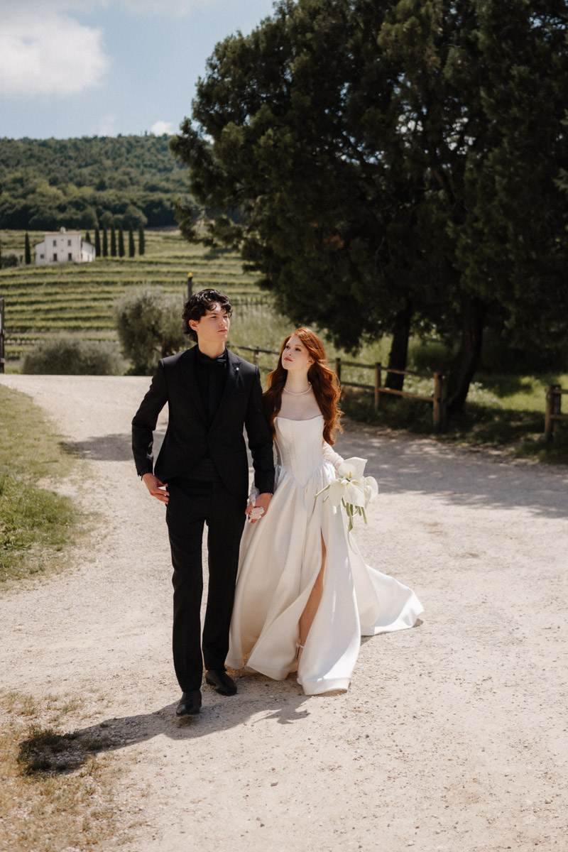 Braut und Bräutigam spazieren Hand in Hand durch Weinberg am Hochzeitstag