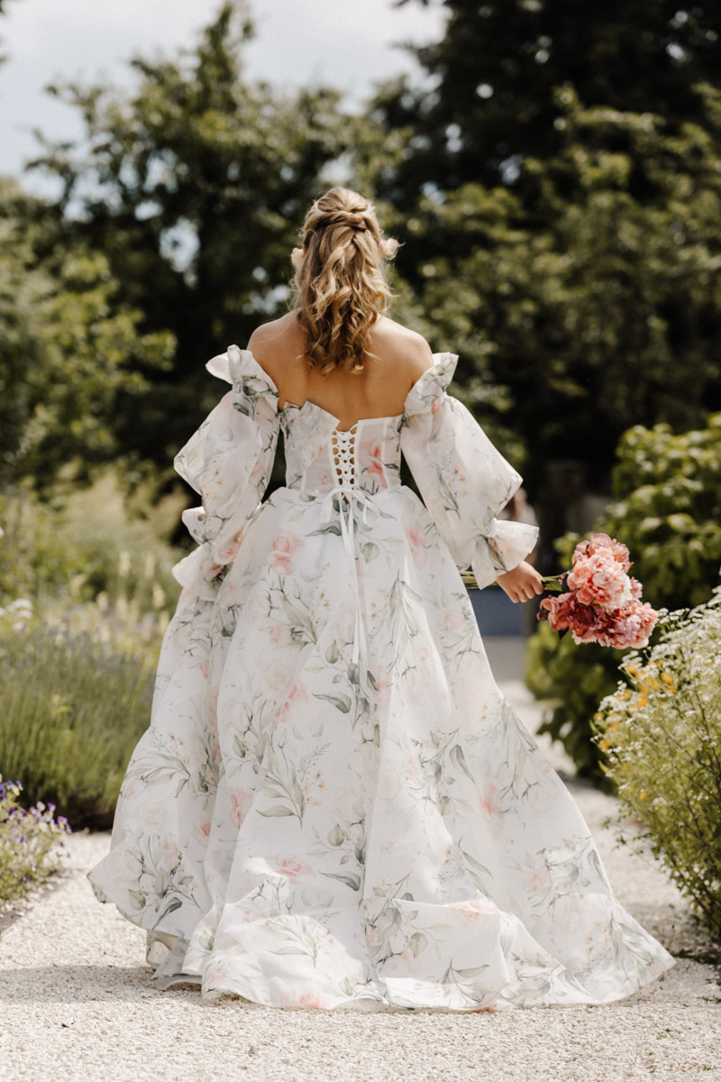Braut in blumenverziertem Hochzeitskleid spaziert durch romantischen Garten