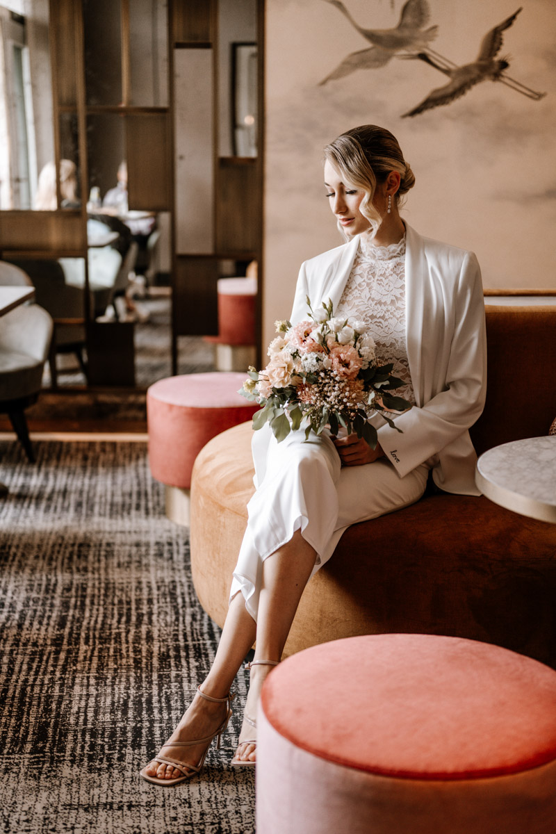 Frau mit Blumenstrauss sitzt mit weissem Blazer auf orangefarbenem Sessel