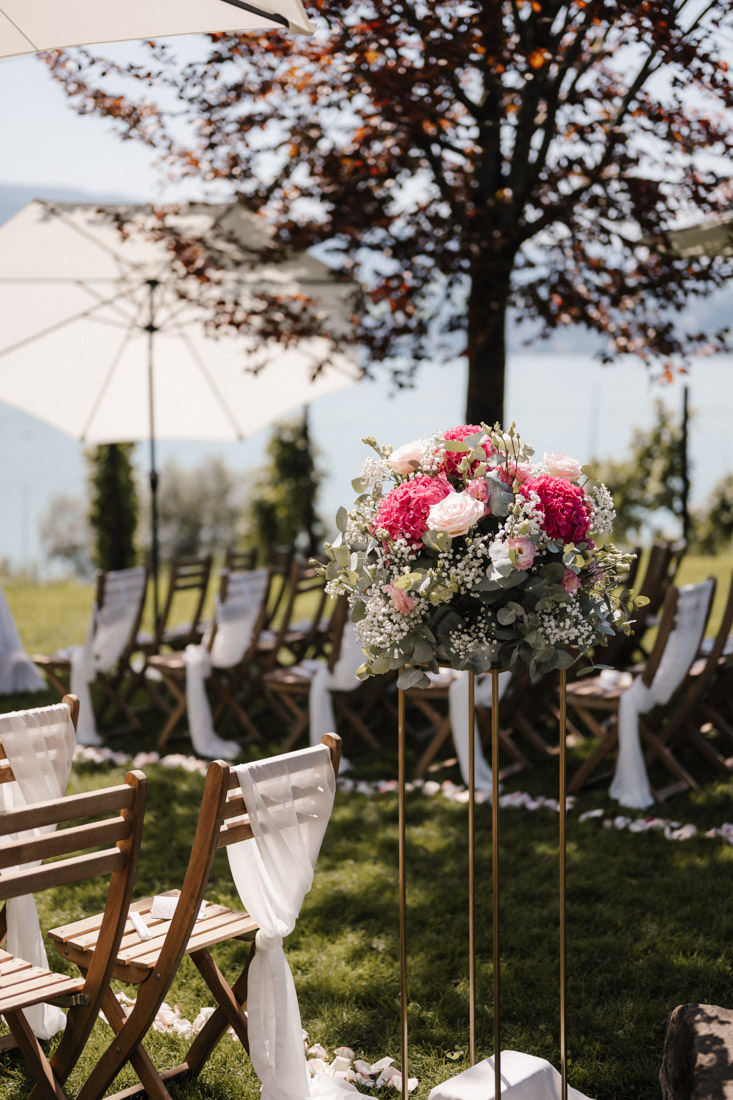 Blumenstrauss auf Goldständer vor Stühlen und See im Hintergrund