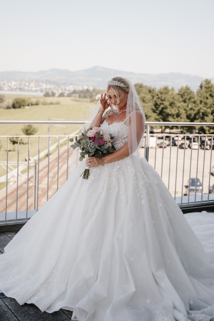 Frau mit Tiara und Schleier hält Blumenstrauss vor See und Bergen