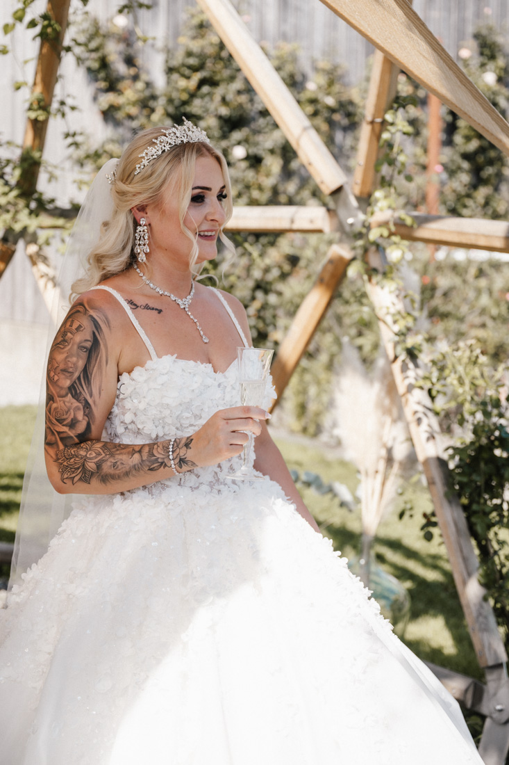 Frau mit Tattoo im weissen Kleid mit Diadem und Sektglas