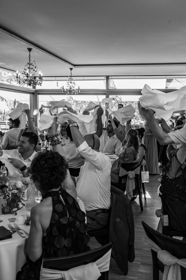 Gäste jubeln mit Servietten in der Luft bei Tisch