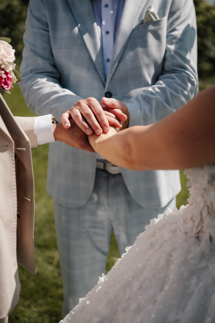 Drei Personen halten Hände mit Anzügen und Brautkleid Details
