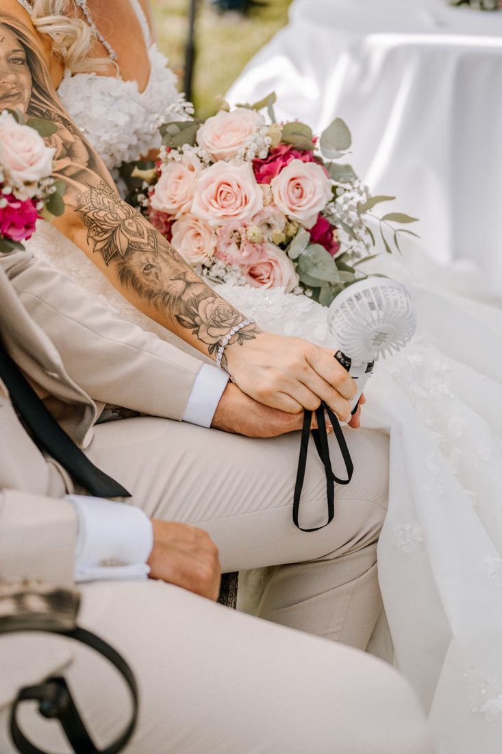 Hände halten sich mit Fächer und Blumenstrauss im Hintergrund