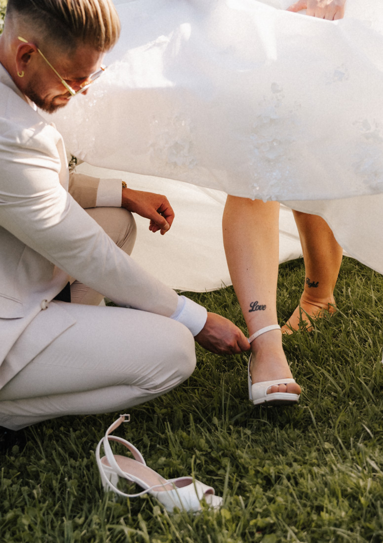 Mann kniet und schliesst Schuh bei Frau mit Tattoo