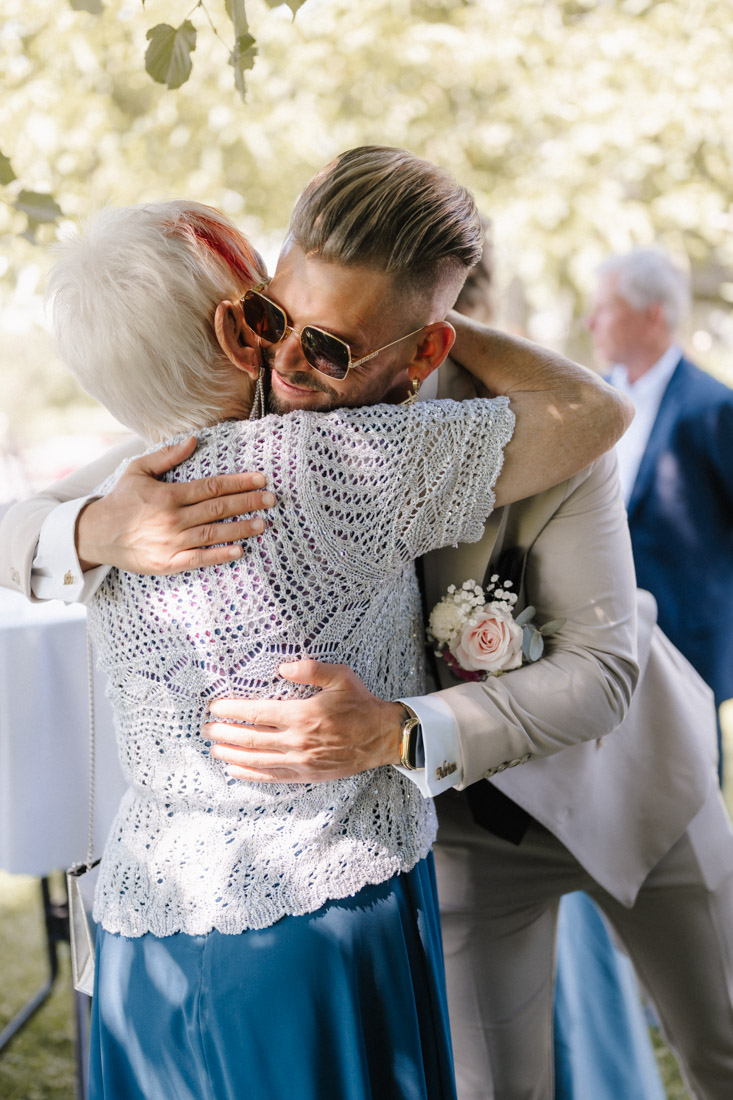 Mann mit Sonnenbrille umarmt ältere Dame mit blauem Rock